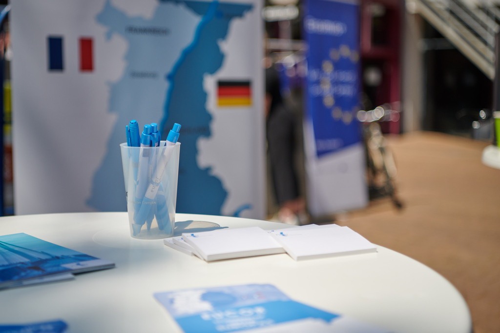 Infostand mit blauen Stiften, Broschüren und Deutschland-Frankreich Karte im Hintergrund.