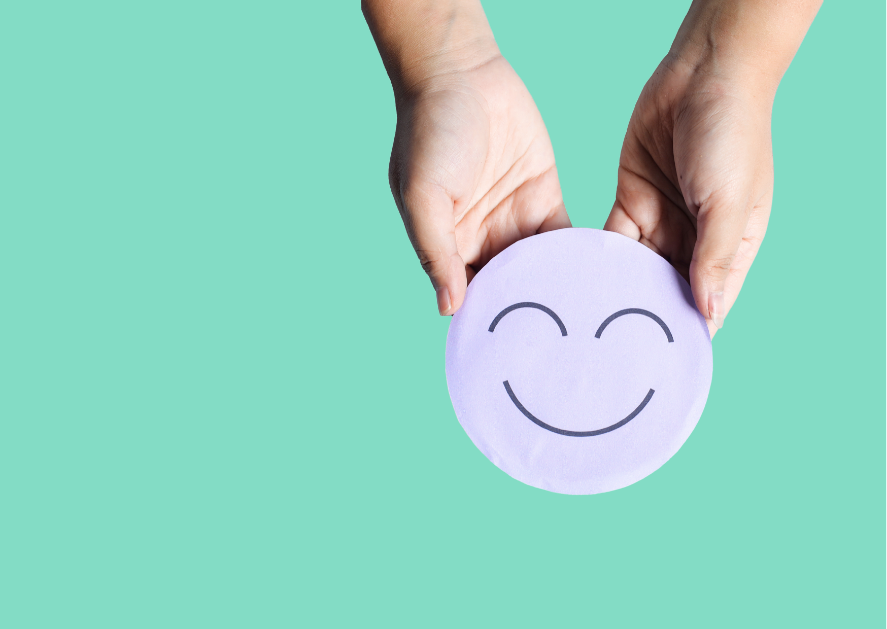 Zwei Hände halten ein violettes Papier mit einem lachenden Smiley-Gesicht vor grünem Hintergrund.