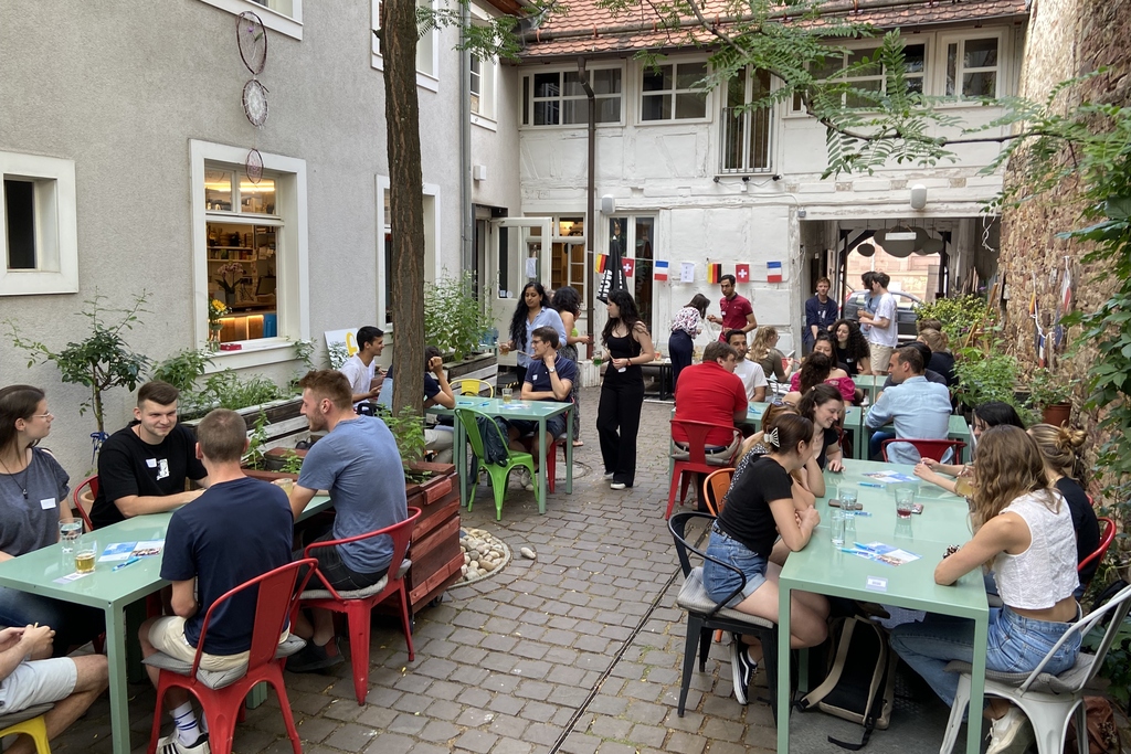 Menschen sitzen in einem gemütlichen Innenhof an Tischen und unterhalten sich.