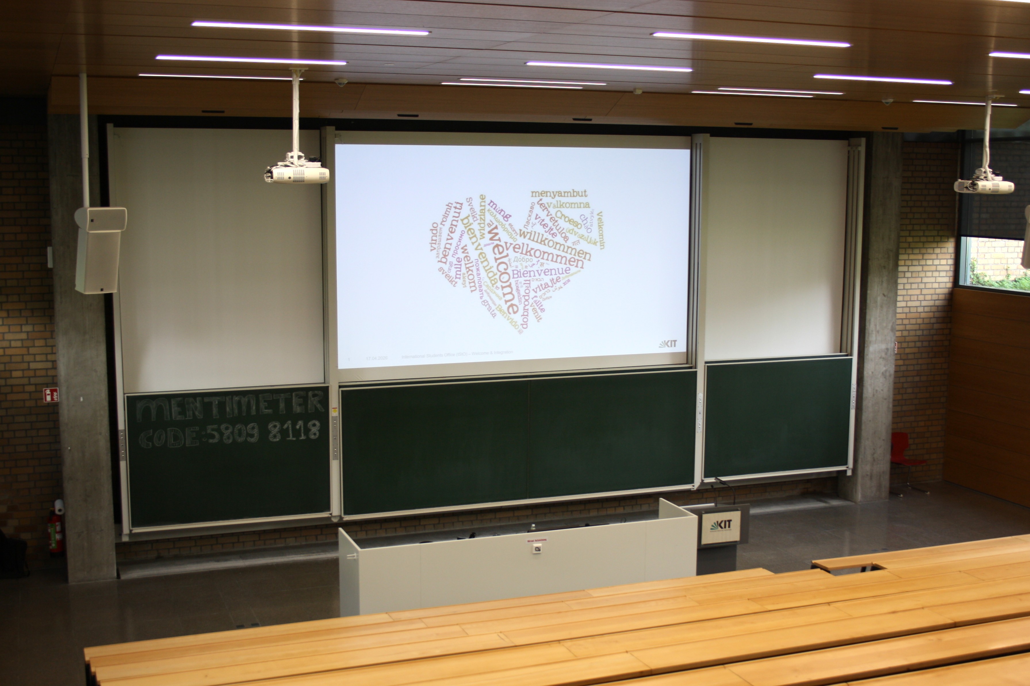 Projektionsleinwand in einem H&ouml;rsaal mit einer Wortwolke in Herzform („Welcome“).