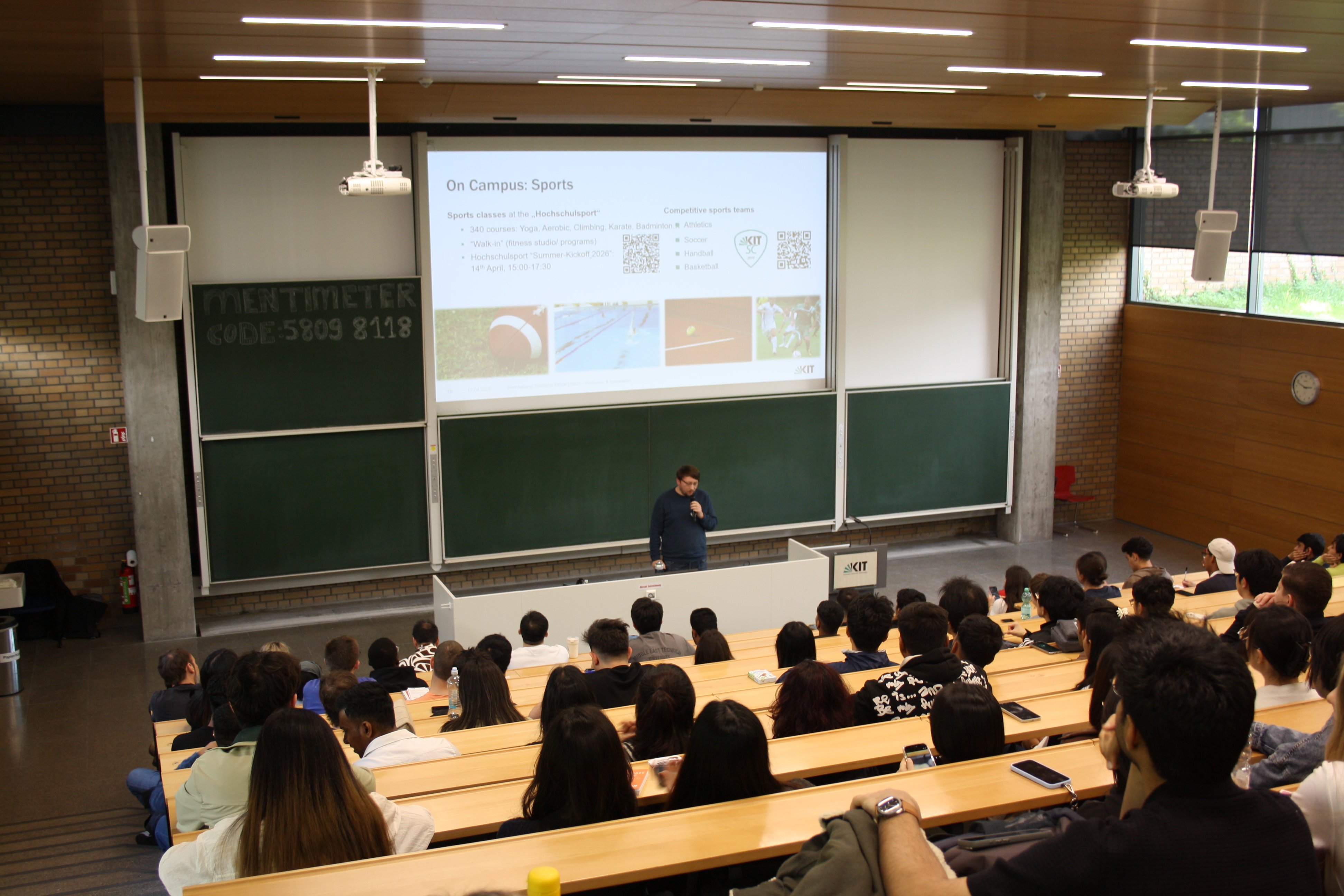 Vortragender vor einem Auditorium und einer Pr&auml;sentationsfl&auml;che zum Thema Campus-Sport.