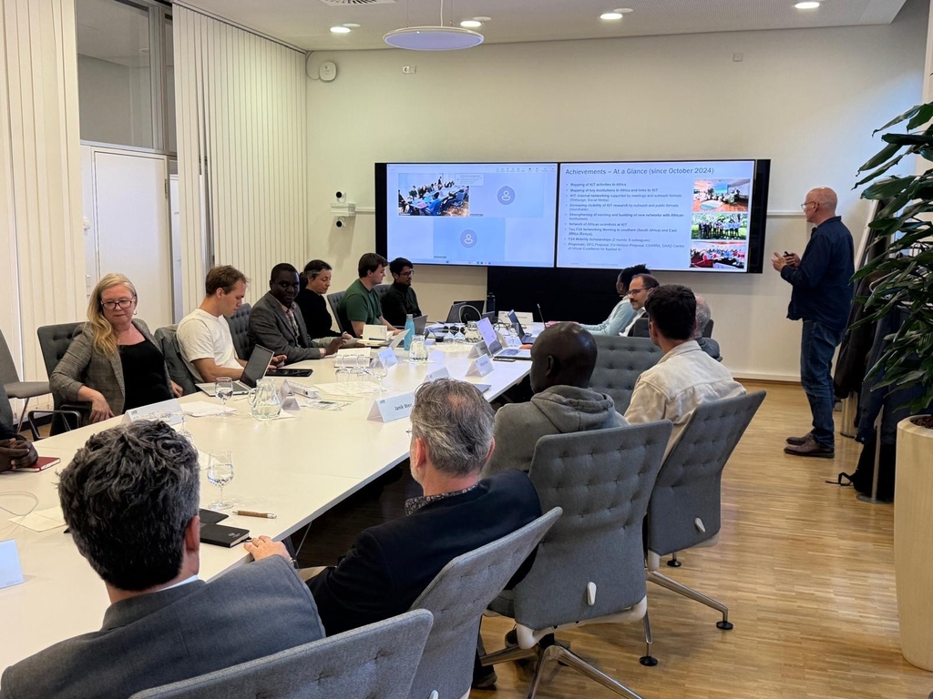 People in a meeting room attending a presentation shown on a large screen.