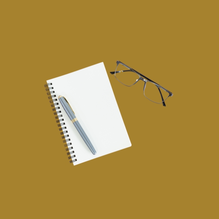 Leerer Notizblock mit Stift und Brille auf senfgelbem Hintergrund.