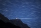 Langzeitaufnahme von Sternenspuren über einer Bergspitze bei Nacht.