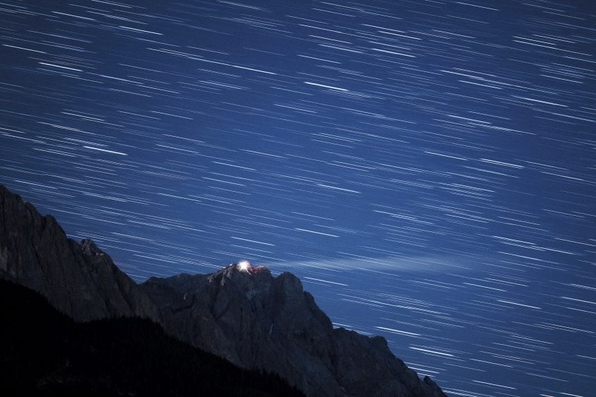 Langzeitaufnahme von Sternenspuren über einer Bergspitze bei Nacht.