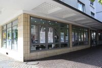 Schaufenster mit Informationsblättern an einem Eckgebäude in einer Fußgängerzone.