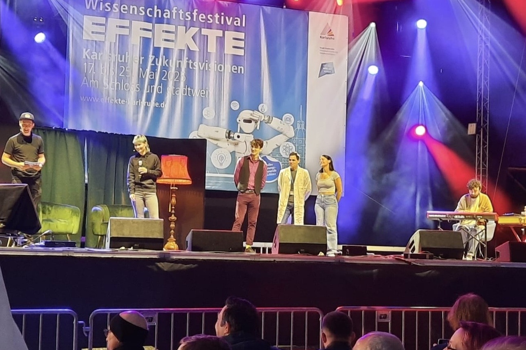 Schaustellerin steht auf Bühne mit Mikro vor Banner „EUCORE SCIENCE SLAM“; Publikum klatscht.