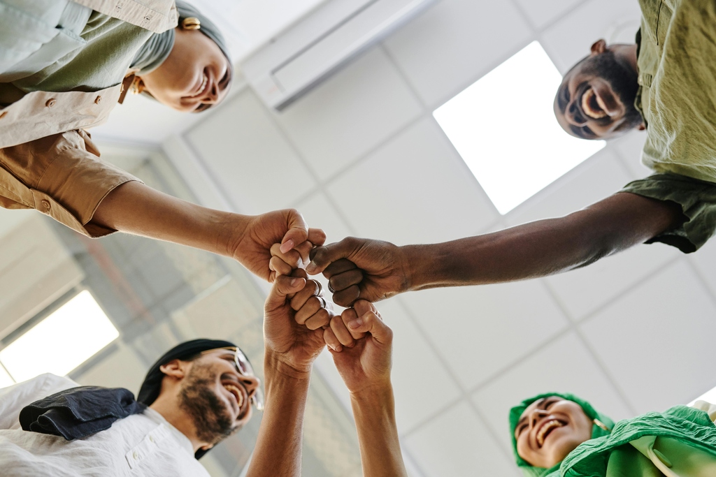 Menschen verschiedener Herkunft zeigen Teamgeist bei einem gemeinsamen Fistbump im Büro.